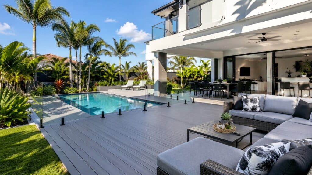 Luxury composite pool deck beside a modern Gold Coast home with glass balustrades and outdoor seating.