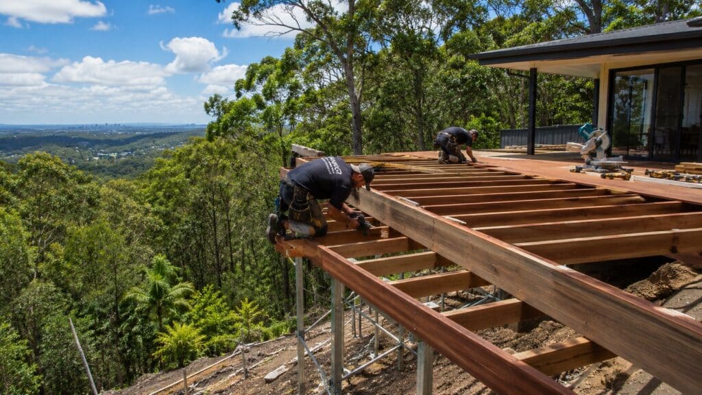 Builders constructing an elevated timber deck on a sloping hillside property in Queensland.