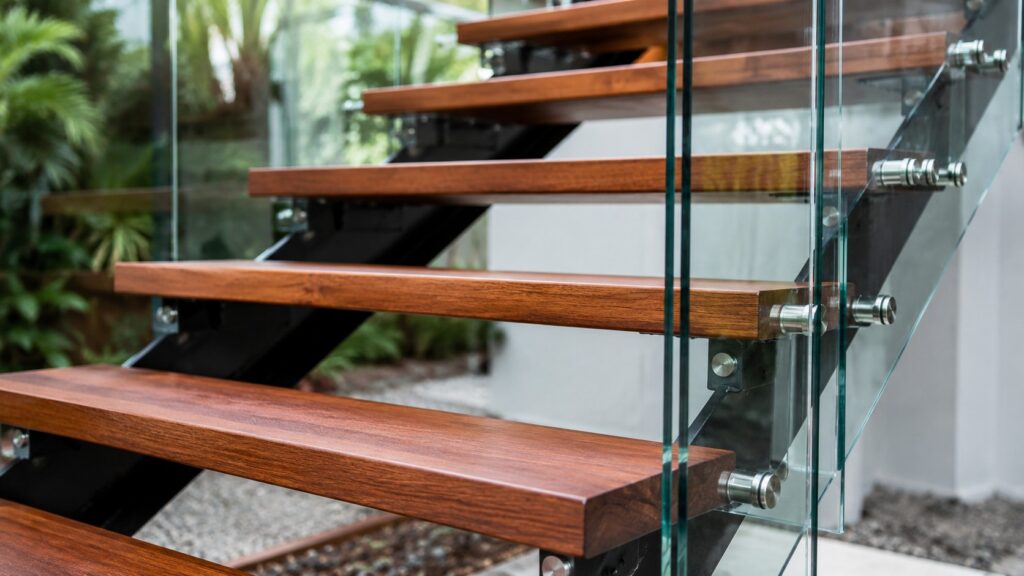 Close-up showing hardwood stairs with steel framing and frameless glass balustrade.