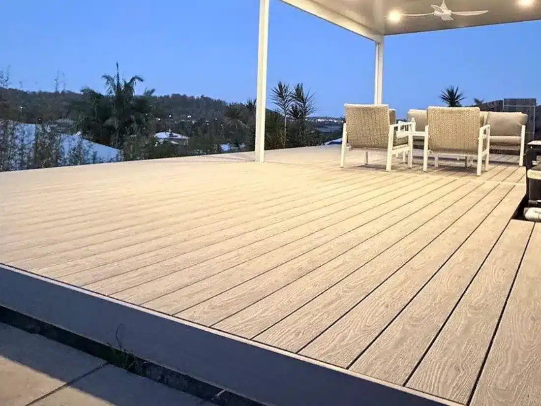Large light grey composite deck under an insulated patio roof with downlights and ceiling fans at dusk