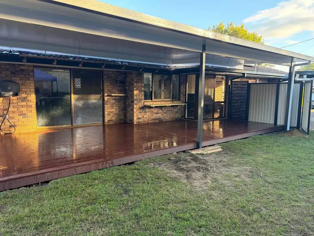 Low set stained timber deck under an insulated patio roof with slat privacy screen